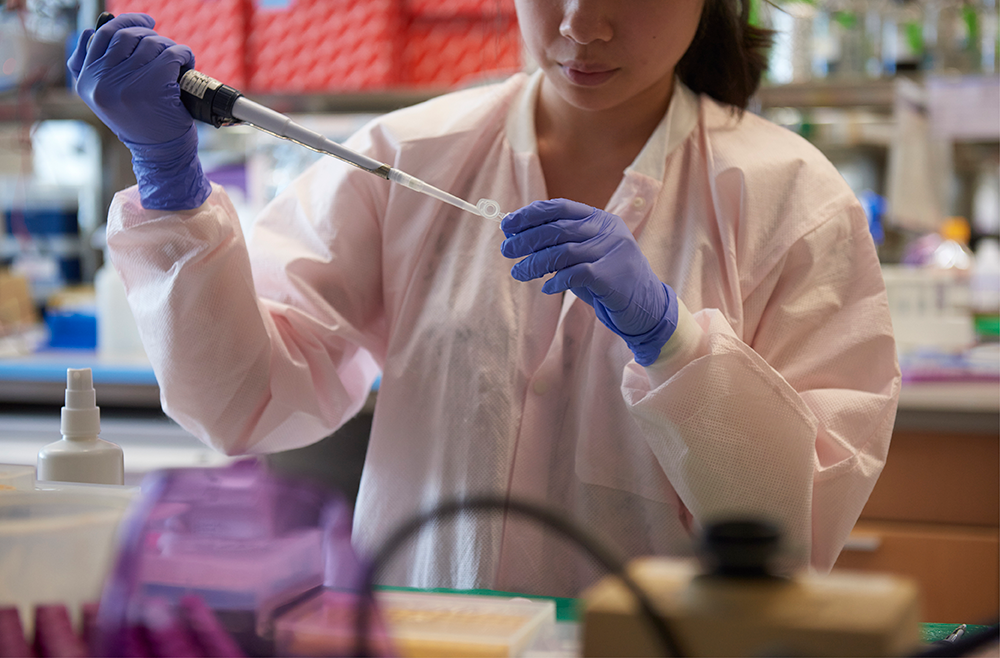 A researcher in a lab coat pipettes a liquid into a vial